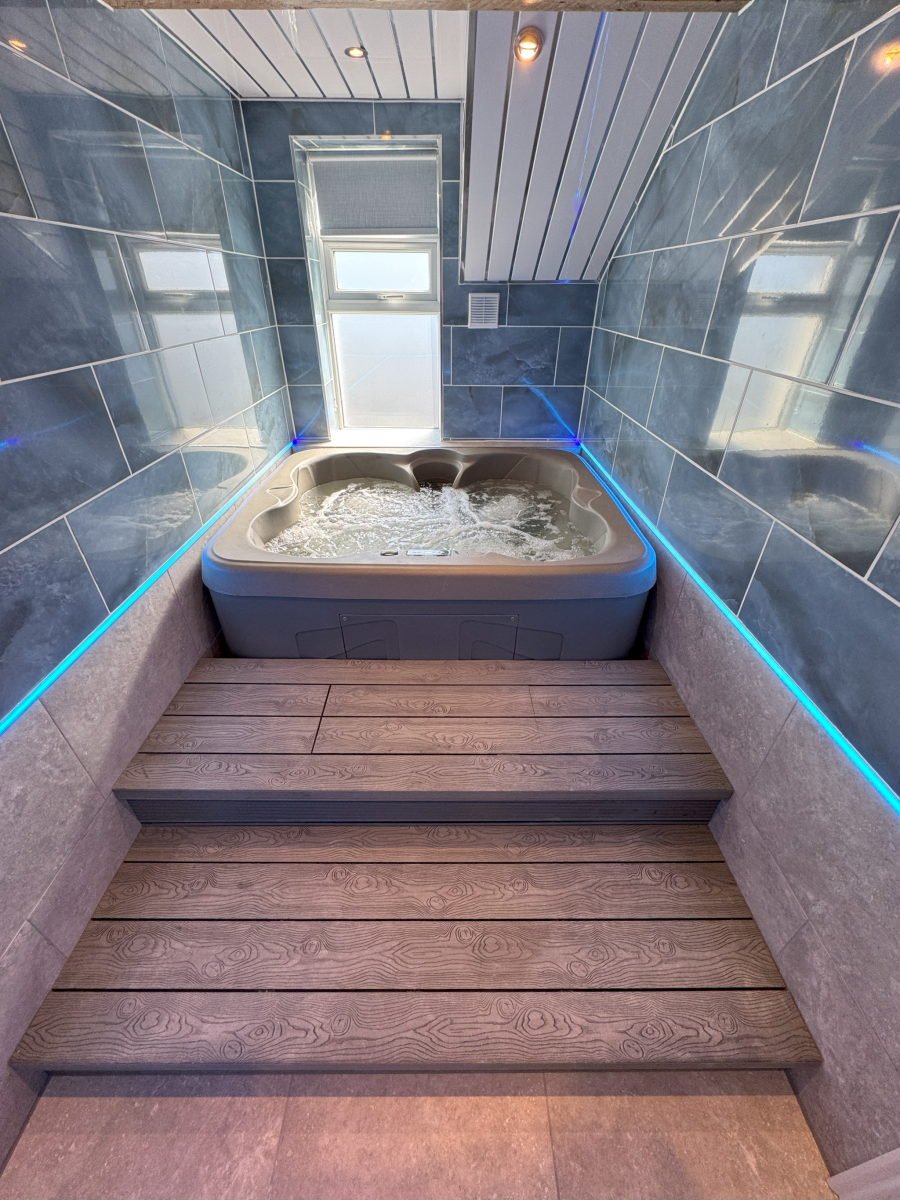 Indoor hot tub in a tiled room with blue LED lighting and wooden steps