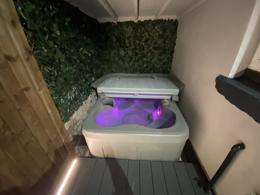 Outdoor hot tub lit purple in a private decked yard with an ivy wall