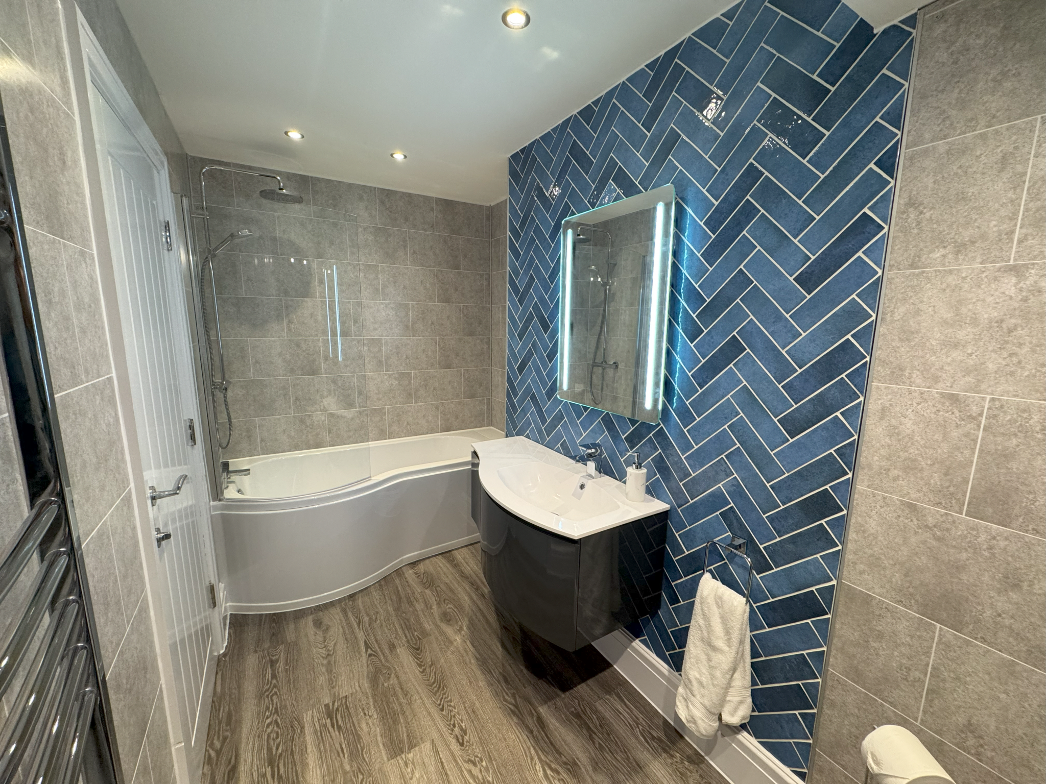 Bathroom with blue herringbone tiles, shower bath and illuminated mirror