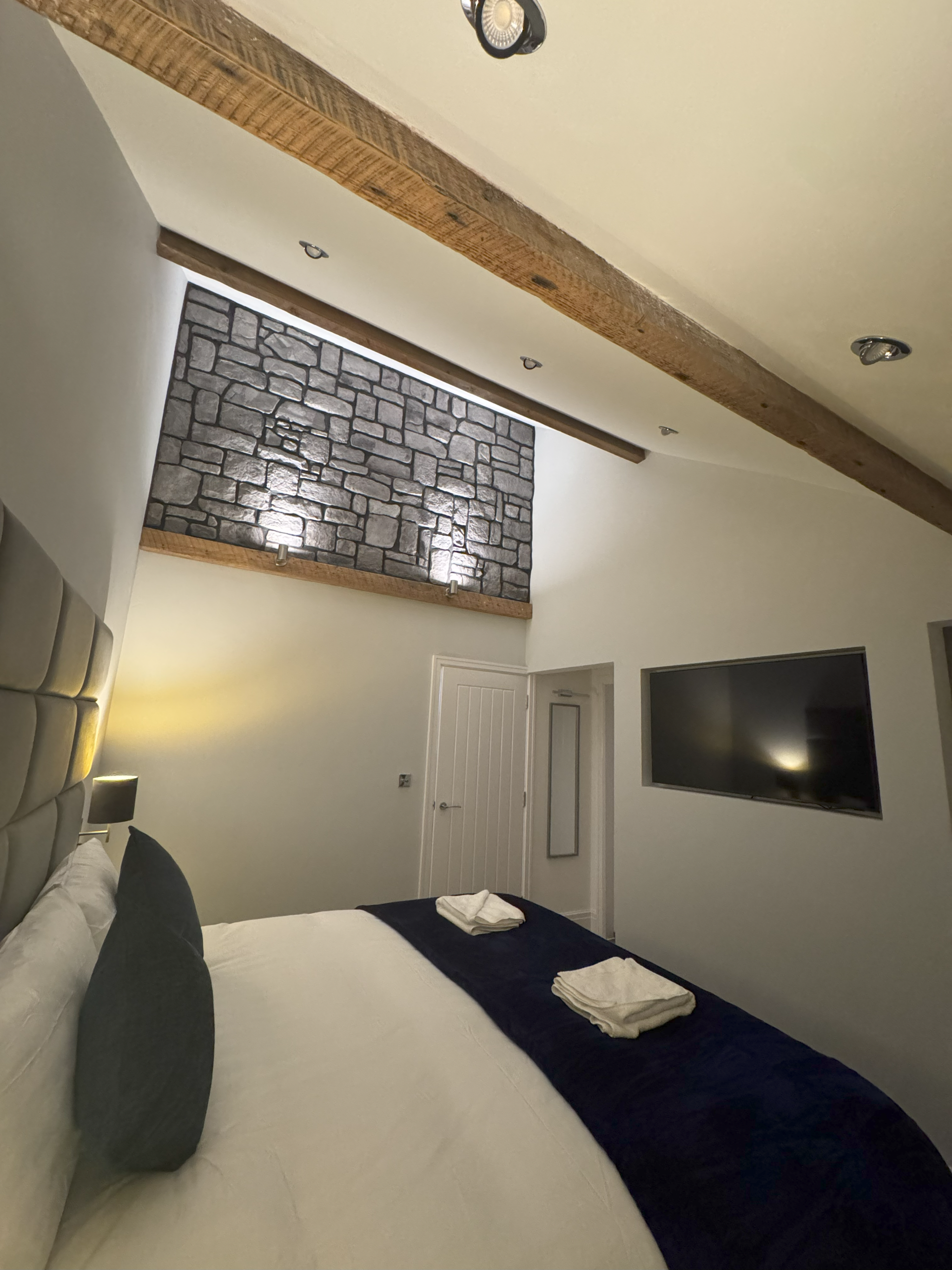 Bedroom with sloped beamed ceiling, stone feature wall and wall-mounted TV