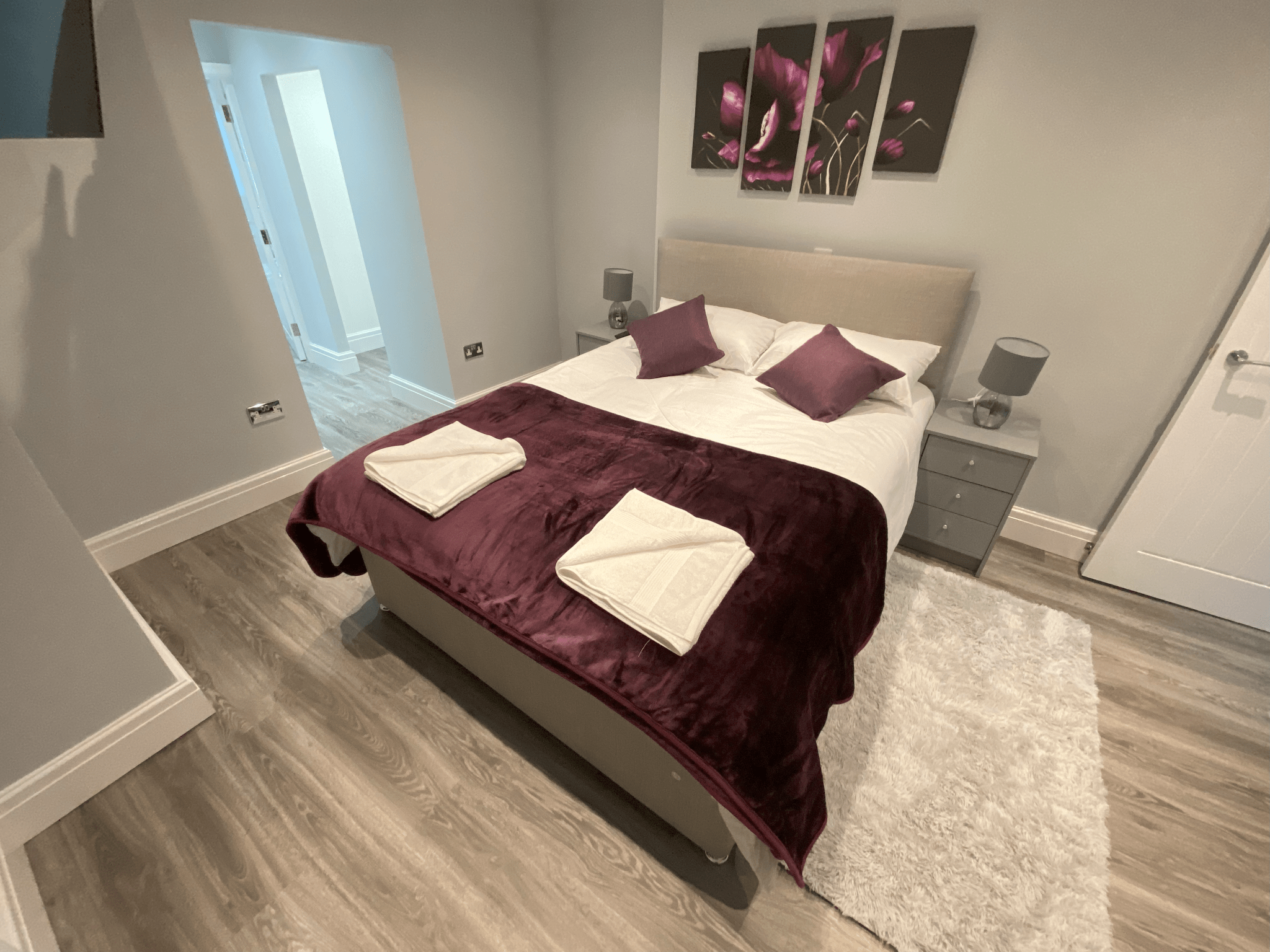 Bedroom with plum throw, cushions and floral wall art