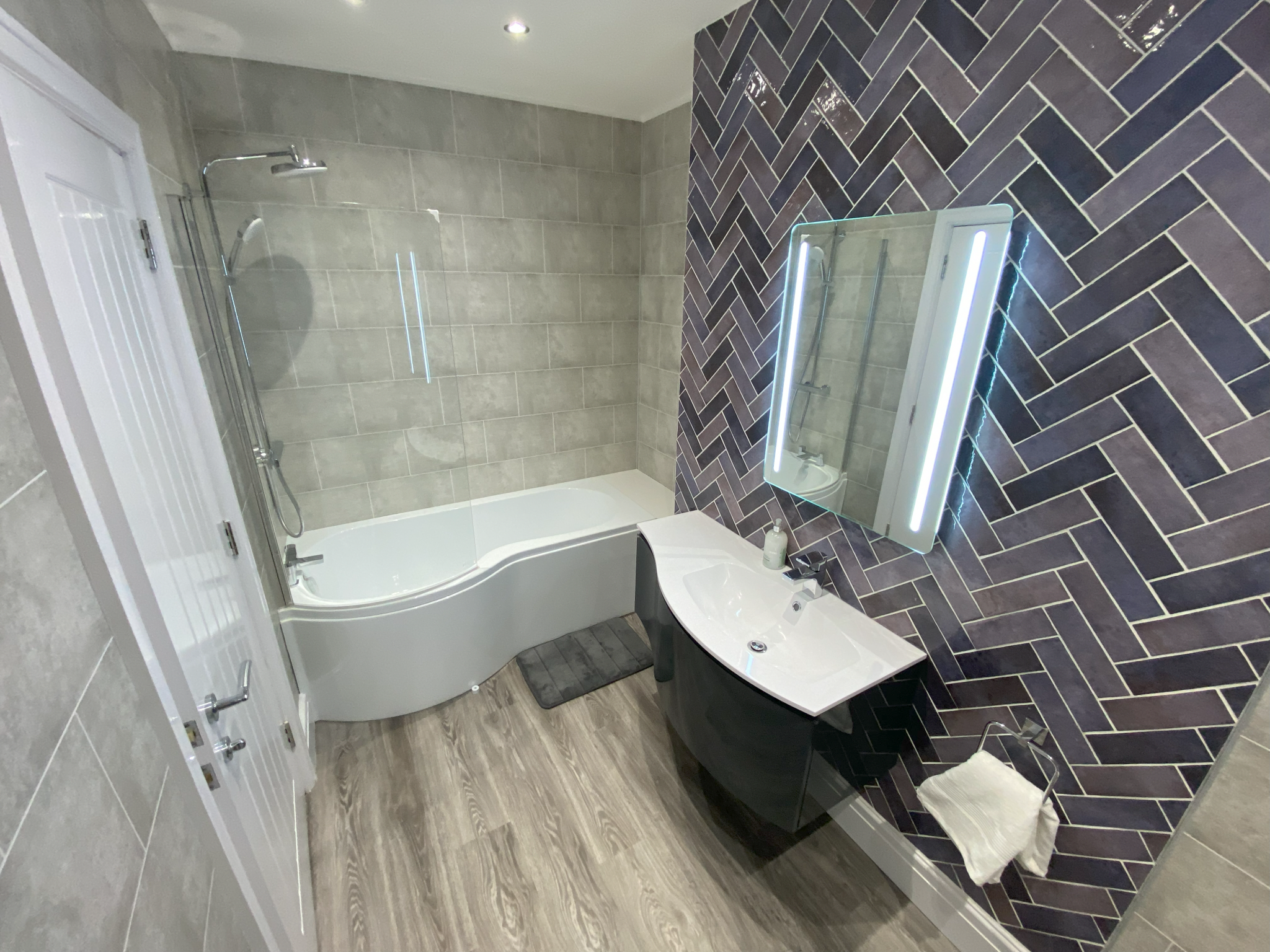 Bathroom with purple herringbone tiles, shower bath and illuminated mirror