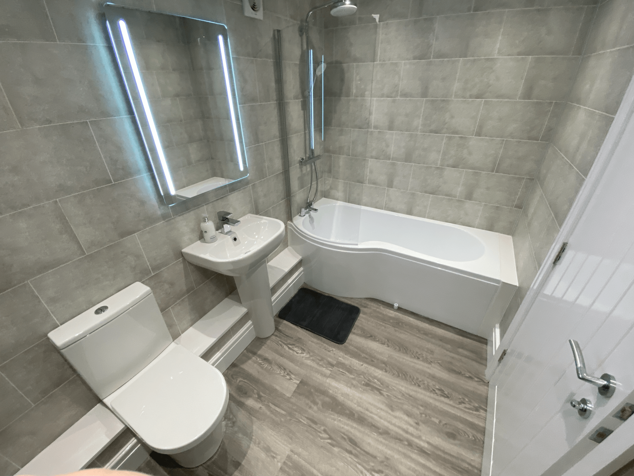 Bathroom with illuminated mirror and P-shaped shower bath